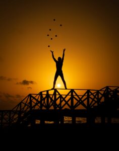 Silhouette of woman with raised arms of freedom standing on bridge during sunset